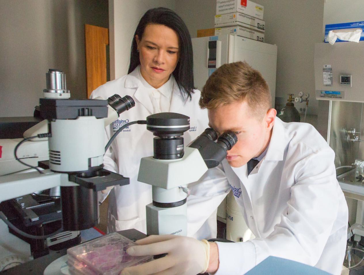 Man looking through microscope with woman observing.